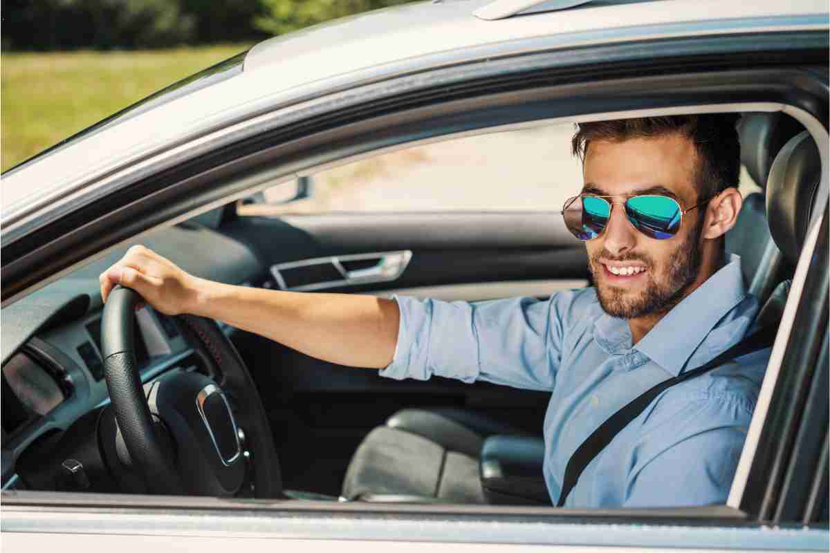 Ragazzo con occhiali da sole seduto in auto che ha noleggiato a lungo termine