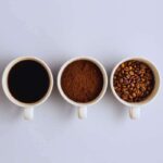 Tre tazzine in fila, una con dentro il caffè liquido, un'altra con dentro quello in polvere e una terza con il caffè ancora in grani