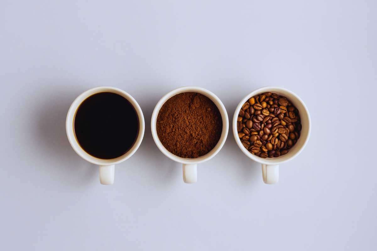 Tre tazzine in fila, una con dentro il caffè liquido, un'altra con dentro quello in polvere e una terza con il caffè ancora in grani